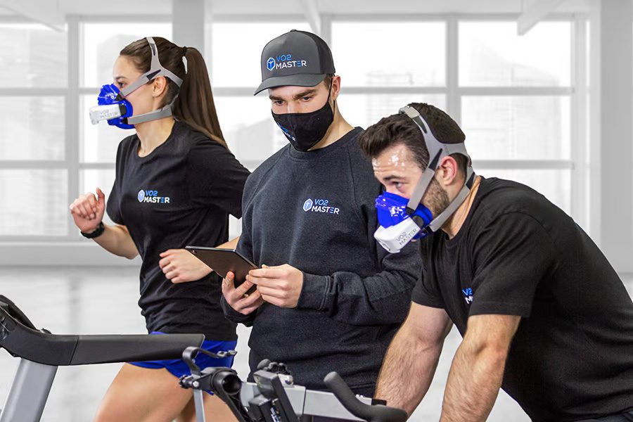 Trainer measuring the performance of 2 athletes inside a fitness research facility, using the blue VO2 analyzer and mask