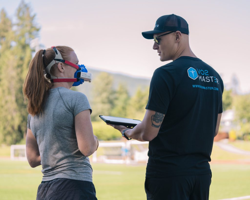 Coaching showing athletic runner their VO2 results on an iPad outdoors while she wears the Analyzer and mask