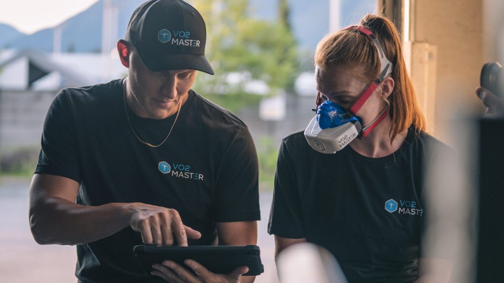 Male coach pointing at tablet with athletic woman wearing the VO2 Master analyzer and mask