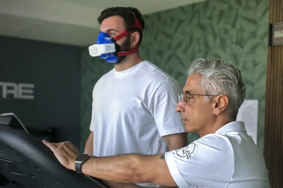 Coach overseeing a treadmill VO2 max test using a portable metabolic analyzer to measure ventilatory thresholds and longevity-focused fitness metrics.