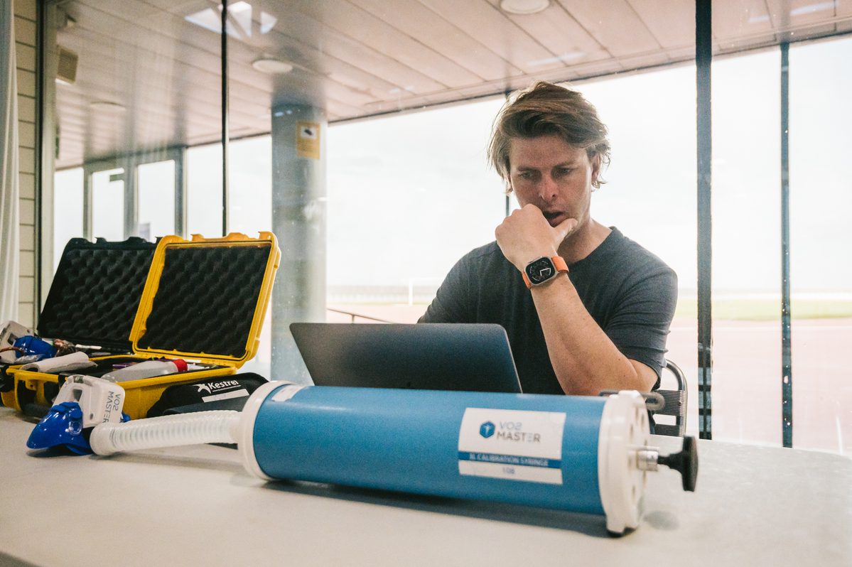 A training coach from the norwegian olympic team is seen analyzing data retrieved from the Vo2 master analyzer during a training session.  He is shown at a table with two analyzer kits and the calibration syringe. 