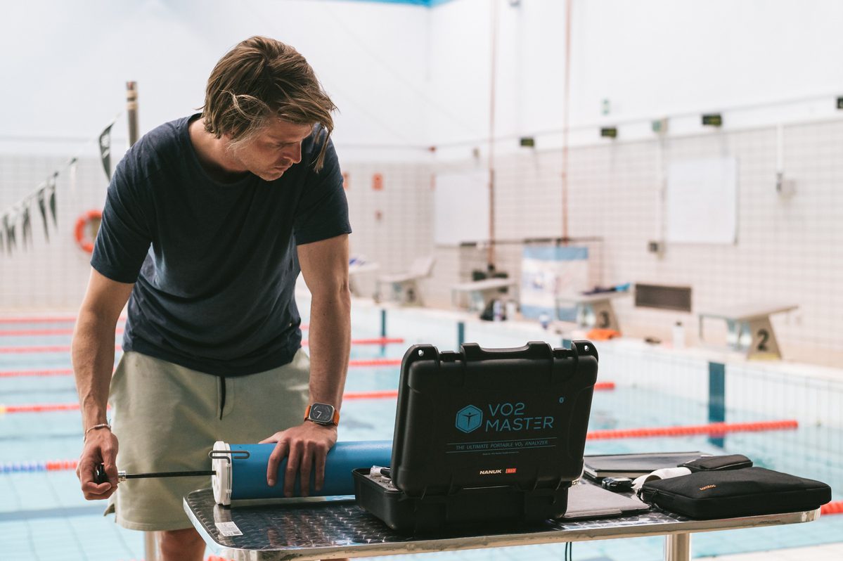 A training coach from the norwegian olympic team is seen preparing the Vo2 master analyzer for a training session.  He is shown at a table with an analyzer kits and the calibration syringe.  He is actively calibrating the device for accurate performance metrics.