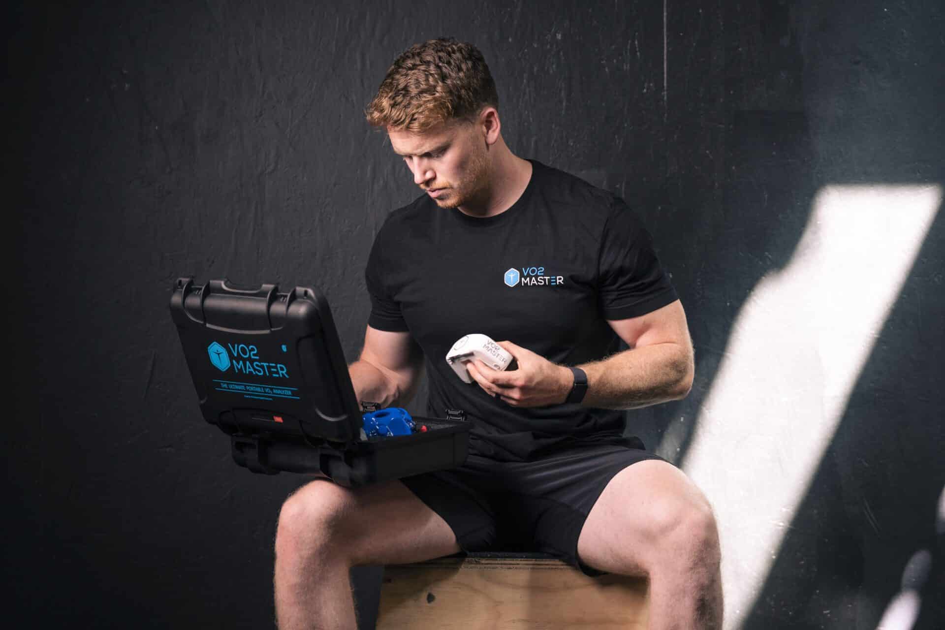 An athletic man sits on a stool examining the contents of the vo2 master analyzer kit reading to track his training metrics and gain new insights on training zones.