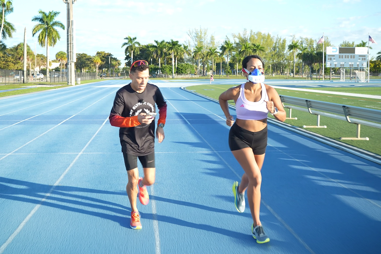 Female runner wearing a VO2 Master mask during a coached submax VO2 testing session on a blue outdoor track.