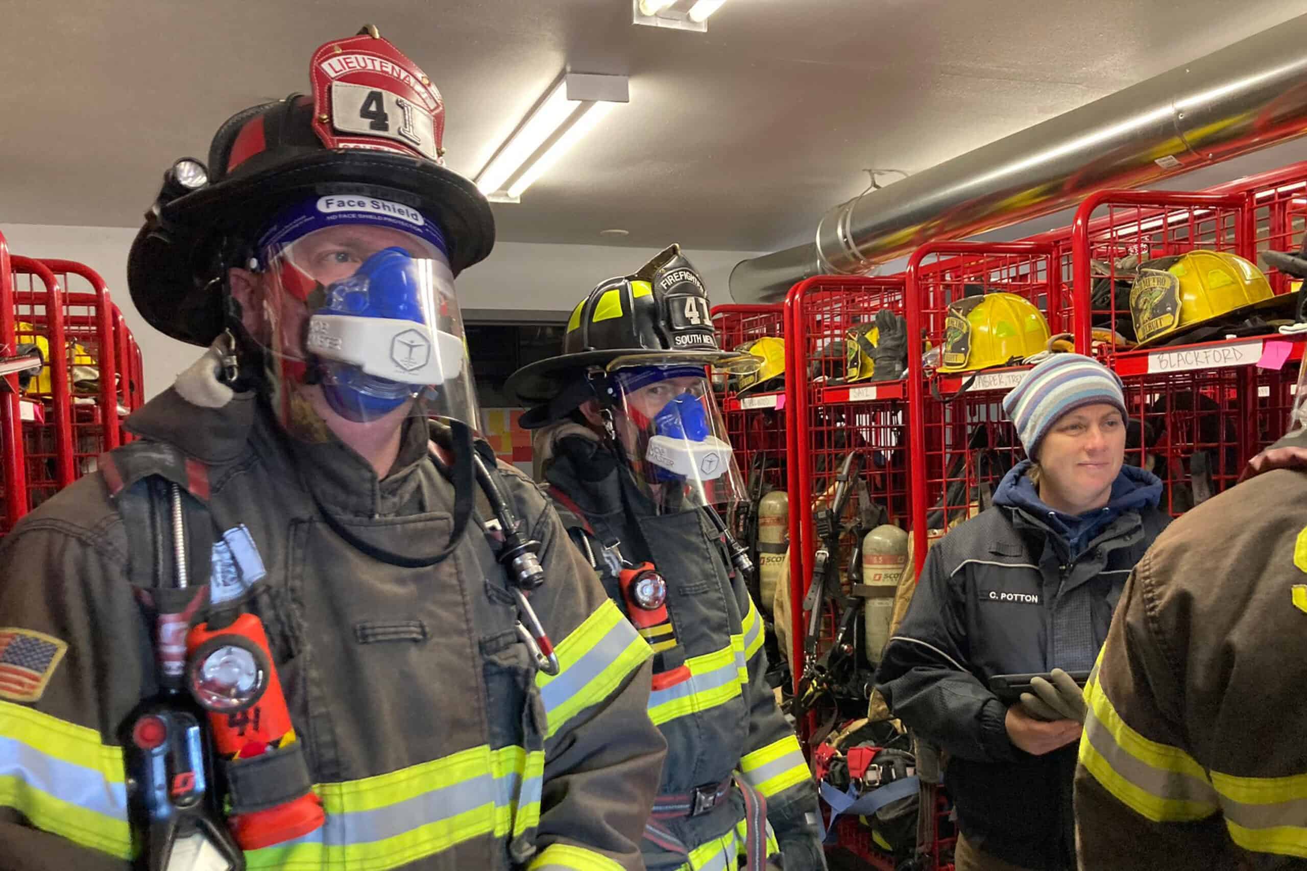 Firefighters wearing VO2 Master Analyzers during indoor readiness assessment, standing in gear room with helmets and SCBA equipment in background.