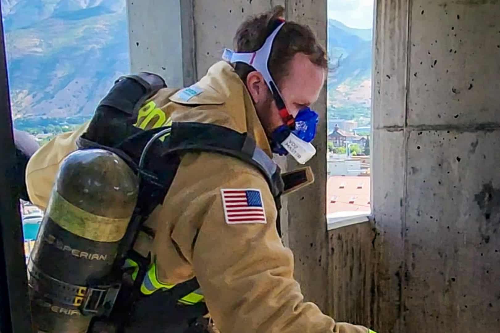 USA firefighter in occupational equipment also wearing a VO2 Master analyzer entering a structure through a window