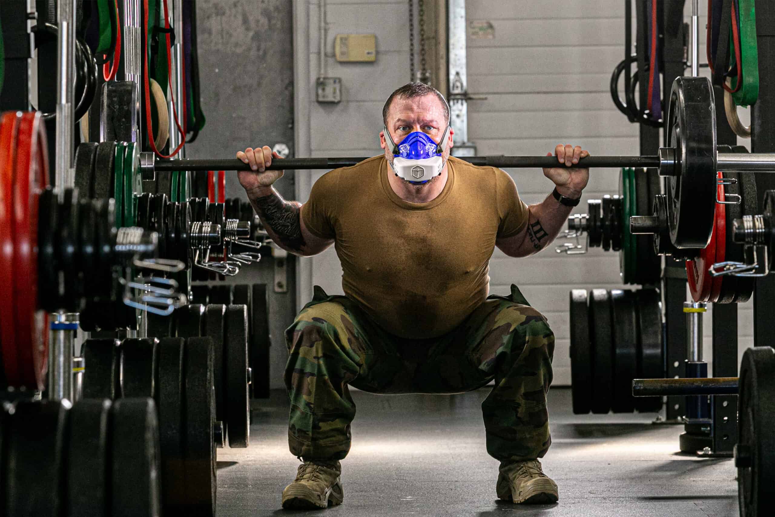 Tactical athlete wearing VO2 Master Analyzer performing barbell squat in weight room to measure metabolic response during strength training.