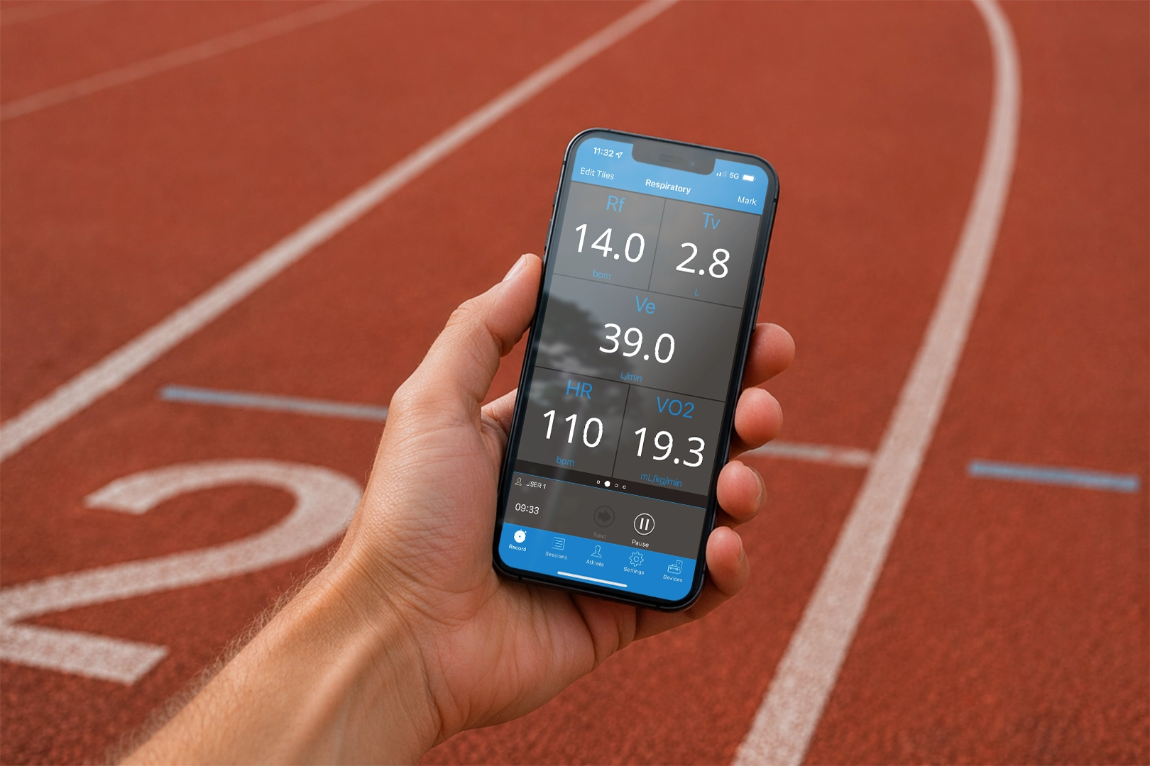 Hand holding a smartphone showing VO2 Master metabolic testing data including respiratory rate, ventilation, heart rate, and VO2 on a running track.