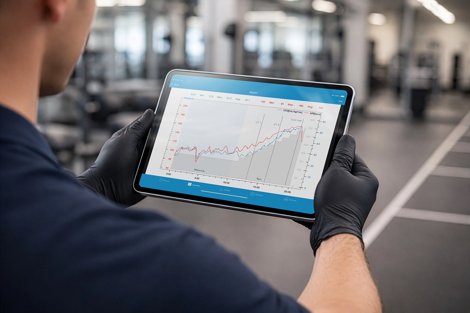 Coach holding a tablet with VO2 Master recovery and heart rate graph in a gym during tactical performance testing.