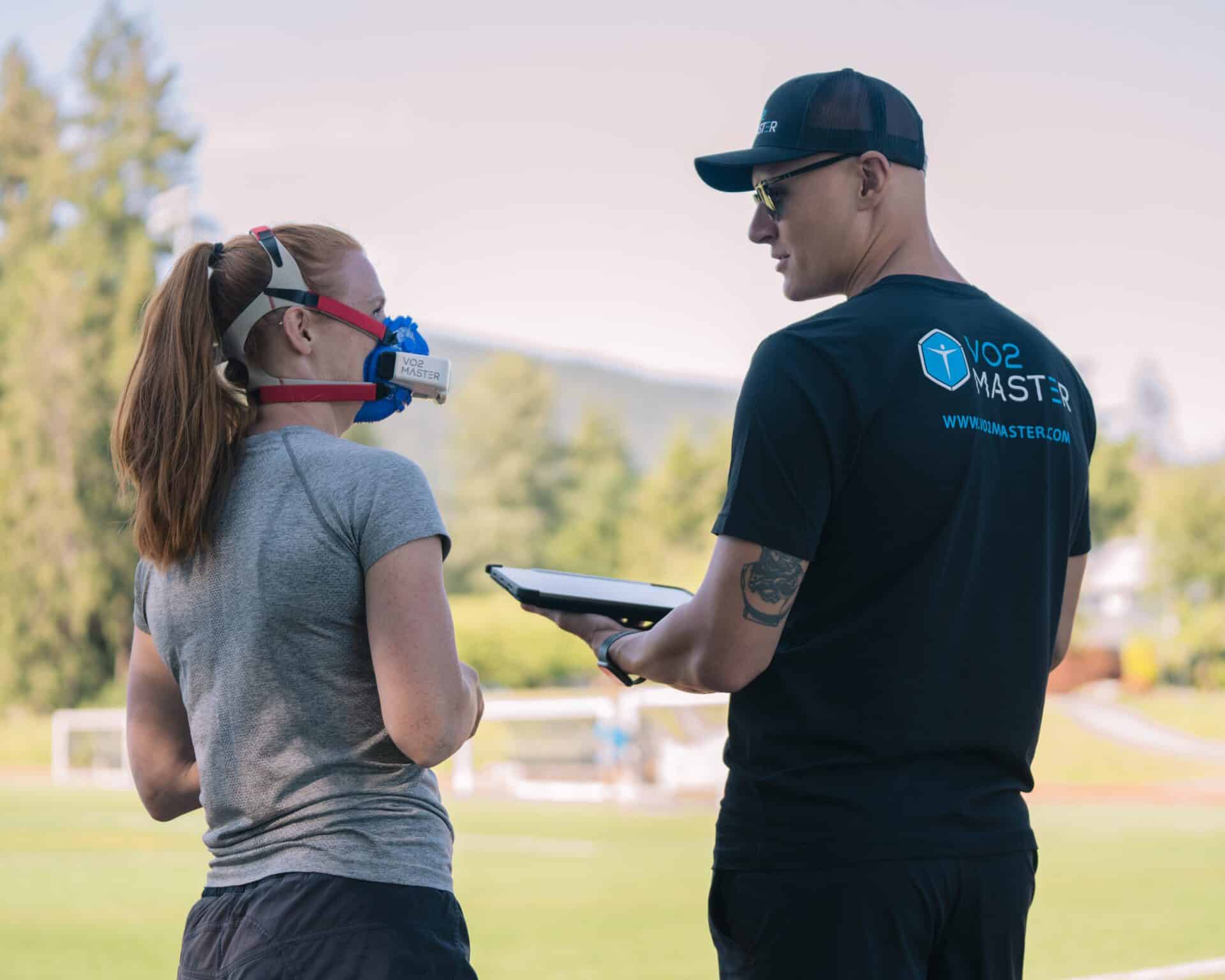 coach stands next to an athlete wearing the vo2 master analyzer preparing to reach peak training zones and track vt1 and vt2 and vo2 max